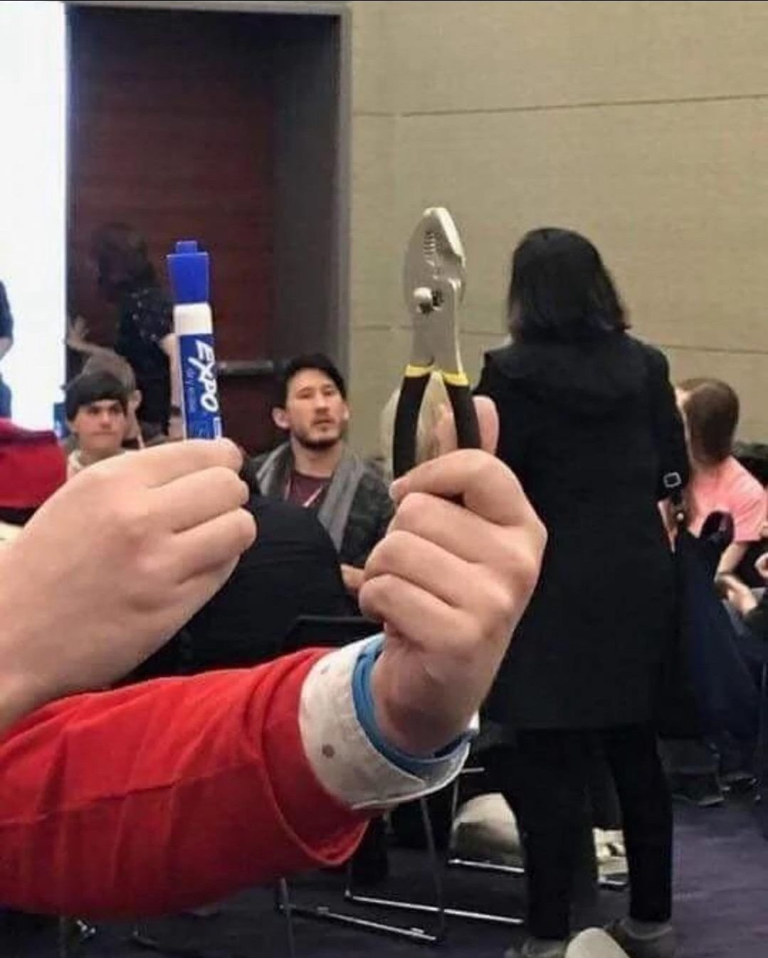 picture of markiplier from far away. in the foreground someone is holding a marker and pliers
